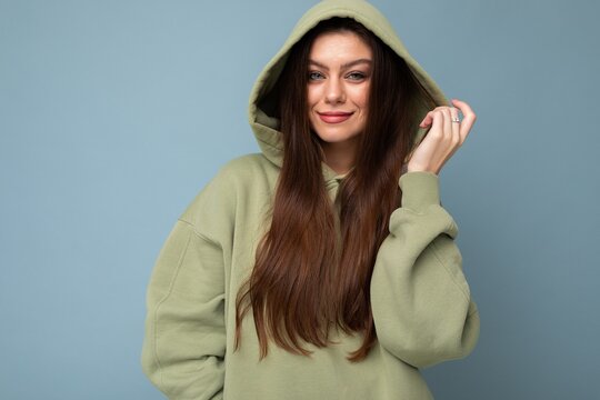 Young beautiful woman looking at camera. Trendy girl in casual hipster hoodie clothes. Positive female shows facial emotions. Funny model isolated on blue background with free space for text