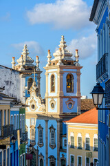 Fototapeta na wymiar Old facades of colorful colonial-style houses, lanterns and windows and a tower of an old baroque church in Pelourinho, the famous historic center of Salvador, Bahia