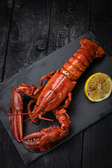 grilled lobster with lemon on a black slate board, on a dark wooden table
