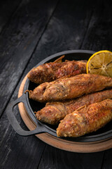 Fried fish on a black cast iron skillet on a dark wooden table

