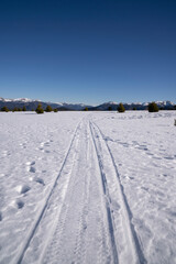Alpine winter landscape. View of the truck tracks across the white field covered with snow in the mountains in a sunny day.