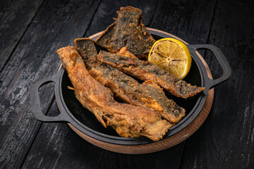 Fried fish on a black cast iron skillet on a dark wooden table
