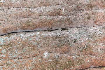 Textured granite surface. Powder with white snow. Horizontal cracks and weathering in stone. Moss and lichen.