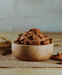 Closeup raw brown Almond seeds in wooden bowl on table with gray background. Macro foods