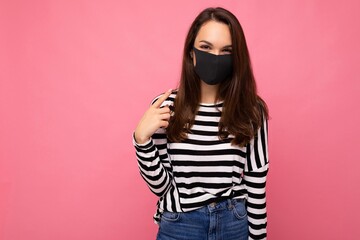 Young woman wearing an anti virus protection mask to prevent others from corona COVID-19 and SARS cov 2 infection isolated over pink background