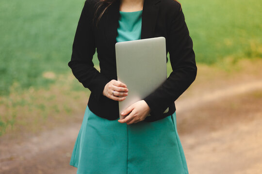 Young business lady in a green dress holds a laptop in her hands. Photo without a head