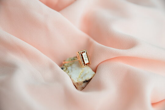 wedding gold ring with orange stone on the white grey stone on a pale pink fabric, a gift for a bride, a girl. photos of jewelry
