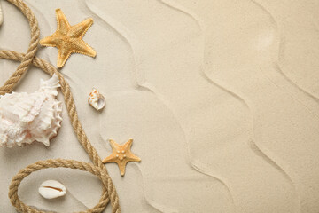 Fototapeta na wymiar Beautiful sea stars, shells and rope on sand, flat lay. Space for text
