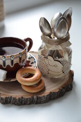a cup of tea in a brown old mug on a wooden stand next to bagels and a jar with a wooden hare from...