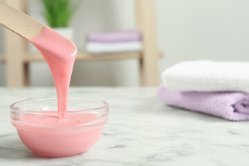 Spatula with wax on white marble table, closeup. Space for text