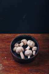 Fresh raw champignon mushrooms in black bowl on wooden background. Autumn harvest, seasonal organic food, healhty eating. Copy space, vertical