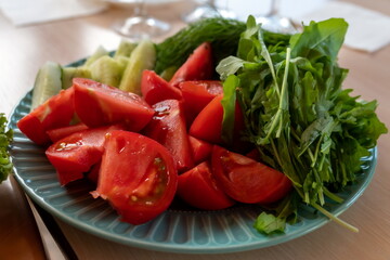 A plate with arugula leaves and slices of fresh tomatoes and cucumbers is on the table.