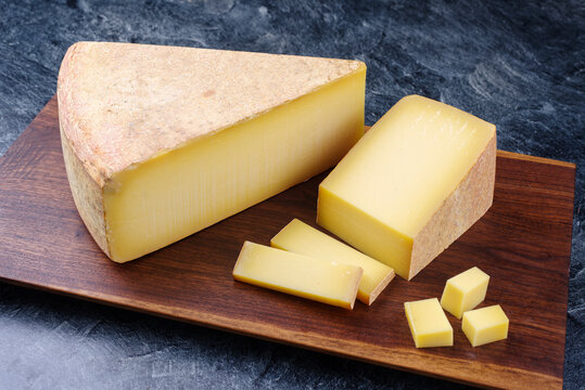 Modern style traditional aged mountain cheese of the Alps offered as piece and slice on a wooden design board