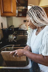 Mujer afroamericana lavando una tabla de picar en la cocina