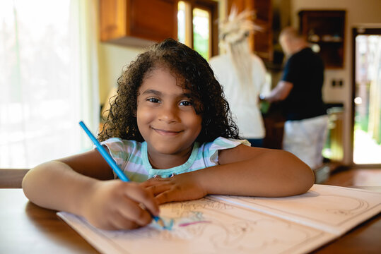 Hermosa ni&ntilde;a morena sonriendo viendo a c&aacute;mara y pintando un libro