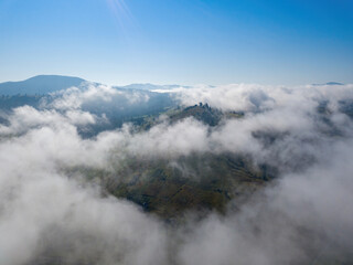 Obraz premium A thin morning fog covers the Ukrainian mountains. Green grass on the slopes of the mountains. A curly thin fog spreads over the mountains. Aerial drone view.