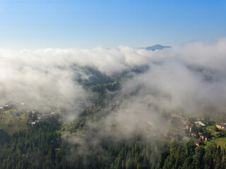 Thin morning fog over a mountain village. Fog covers the Ukrainian slopes of the mountains. Aerial drone view.