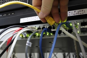 Close-up of a hand that connects a UTP cable to the switch. View from below. Yellow computer...