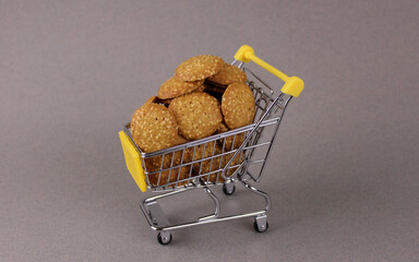 Cookies in miniature shopping cart on gray background