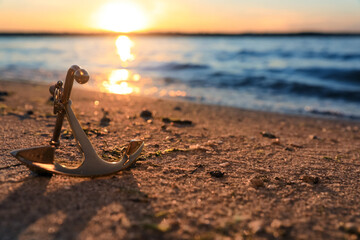 Metal anchor on shore near river at sunset