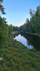 a slow flowing river in a windless tree valley with blue skies and green grass