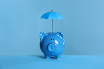 Small umbrella and piggy bank on light blue background