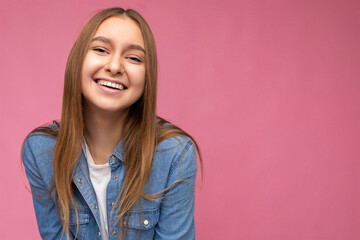 Fototapeta premium Closeup of positive smiling happy young charming nice pretty dark blonde woman with sincere emotions wearing hipster blue jean shirt and casual white t-shirt isolated over pink background with free