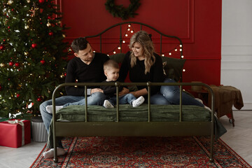 Young traditional couple with little cute son posing near Christmas tree in the decorated for New Year interior. Traditional family spending Christmas time together