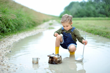 A boy, 8 years old, is playing in a big puddle. Concept of a happy childhood.