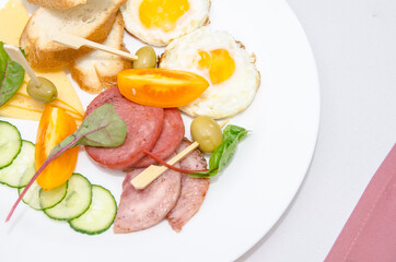 fried eggs with bacon orange tomatos bread cucumber and olive and vegetables on a white plate close up