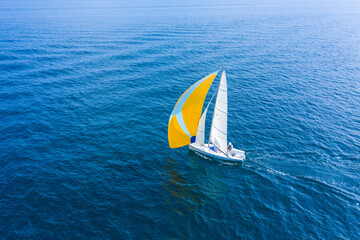 Aerial view of a beautiful white sailing yacht with a colored sail.
