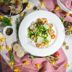 salad with shrimps in white plate on the table with a white tablecloth and pink napkins decorated for Christmas