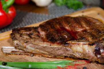 lamb steak with blood on the bone on a wooden board with green onions and red sauce close up