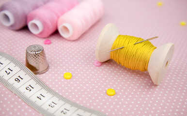 Fototapeta na wymiar pink cotton fabric, a spool of yellow thread, a needle and a thimble. Sewing accessories