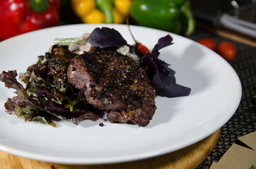 beef steak with black pepper on a white plate decorated with greens on a wooden table