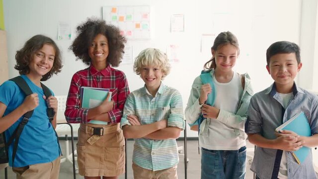 Portrait of cheerful smiling diverse multiethnic elementary school children standing posing in classroom looking at camera happy after school reopen. Diversity. Back to school concept.