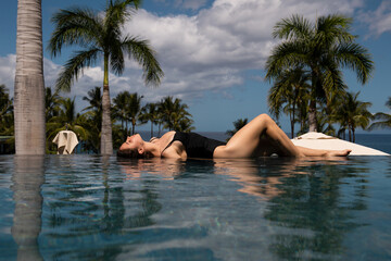 Sexy elegant woman in infinity pool and enjoys the view over the blue sea.