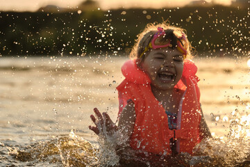 Little girl plays in the river lake. Golden hour. A child splashes water on the beach during summer vacation. Safety on the water.
