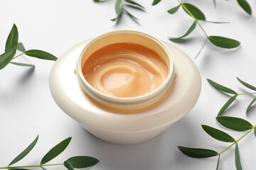 Jar of hair care cosmetic product and green leaves on white background, closeup