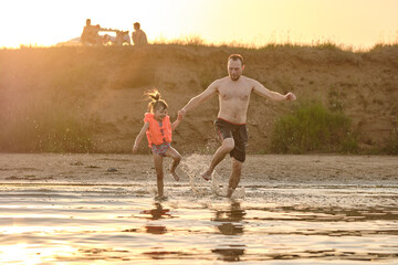 Daughter with her father plays in the river lake. A child in a life jacket. Safety on the water....