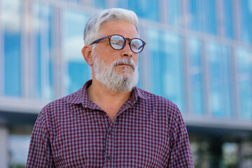 an adult gray-haired man with a beard goes to the office to work. a senior businessman in a shirt and with a laptop is making a career in a large company. a stylish European talks on the phone with