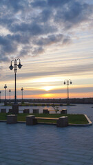 Fototapeta na wymiar landscape sunset river orange light clouds summer autumn embankment lanterns benches