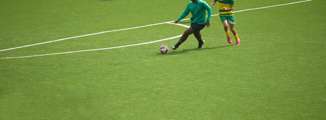 Dois jogadores a jogar futebol e a disputar a posse de bola - equipamentos verde e preto e amarelo...