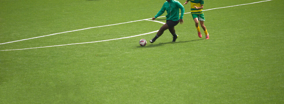 Dois jogadores a jogar futebol e a disputar a posse de bola - equipamentos verde e preto e amarelo e verde - casaco vestido