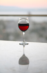 A glass of red wine with its reflection on table at sun set view.