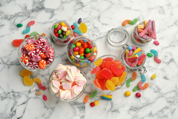 Obraz na płótnie Canvas Jars with different delicious candies on white marble table, flat lay