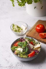 A small white salad bowl with microgreens, cherry tomatoes and fresh basil leaves on a wooden board on a grey concrete surface