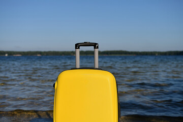 Yellow suitcase on the background of blue sea. Relax time, holiday concept. Copy space