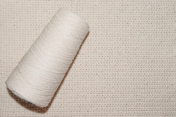 Fototapeta na wymiar Beige spool of thread on the knitted napkin background