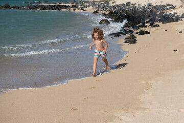 Child running through water close to shore along the sea beach. A boy runs along the sea coast. Rest of children on summer vacation.